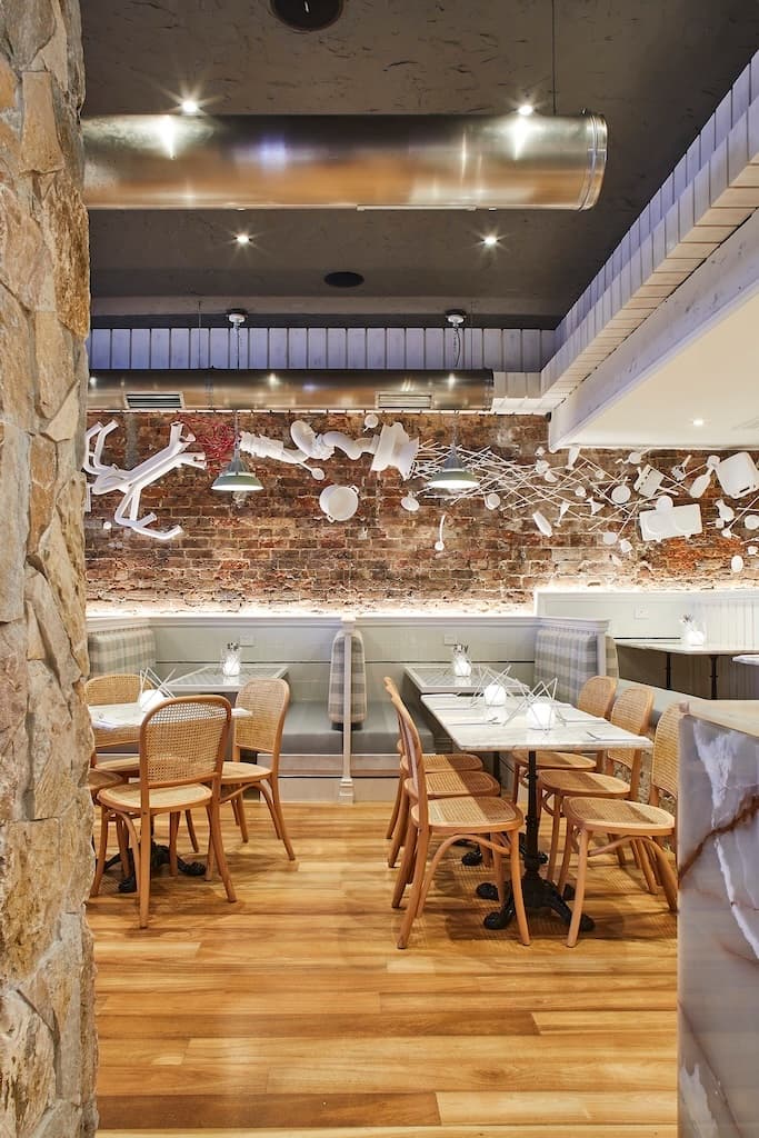 A dining area with a mix of booth and regular seating, showcasing modern decor with unique white kitchen utensils on a brick wall, creating a trendy and eclectic atmosphere